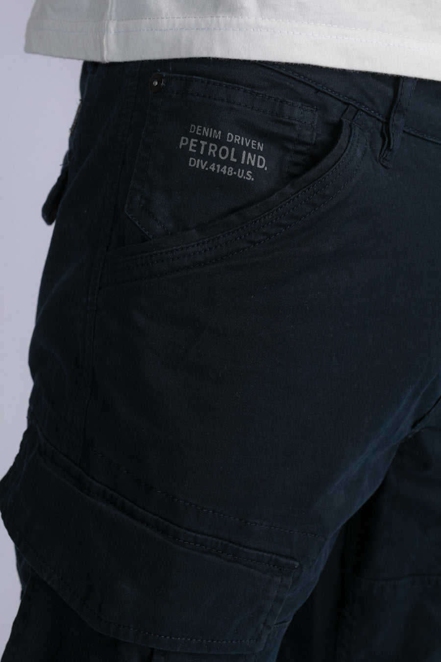 Blauwe cargobroek van Petrol Industries, met klepzak en stikseldetails, gedragen met een wit T-shirt.