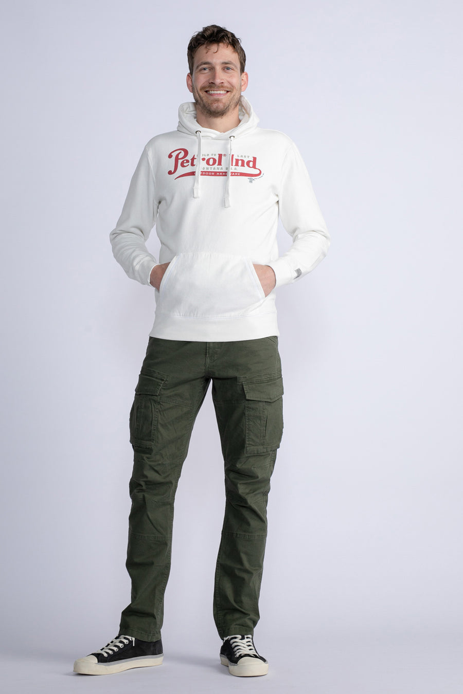 Groene cargobroek van Petrol Industries, met klepzakken, gedragen met een witte hoodie en zwarte sneakers.