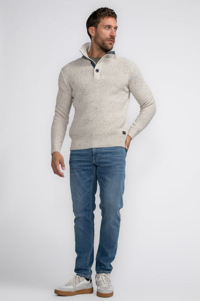 Pull à col roulé écru de Petrol Industries, avec deux boutons au col, porté avec un jean bleu et des baskets blanches.