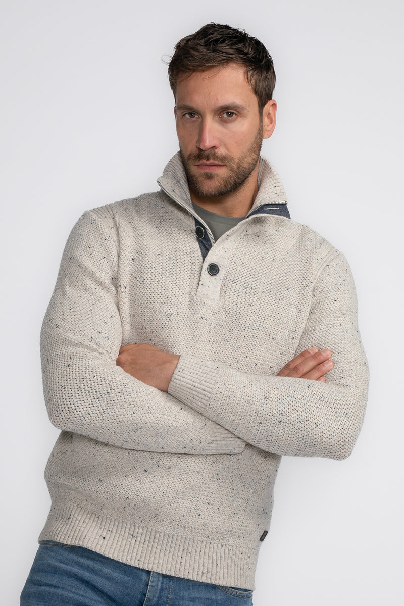 Pull à col roulé écru de Petrol Industries, avec texture tricotée, col montant boutonné et porté avec un jean bleu.