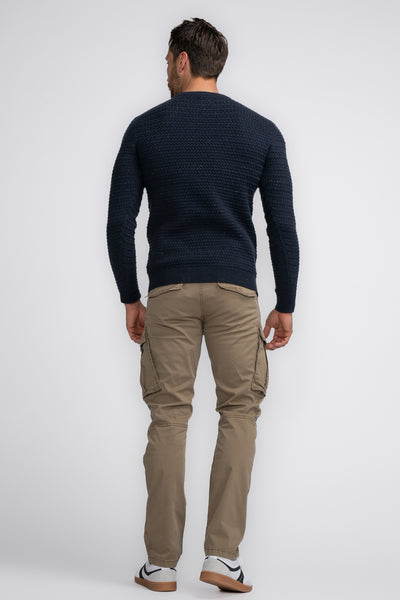 Pull à col rond bleu de Petrol Industries, porté avec un pantalon cargo beige et des baskets blanches.