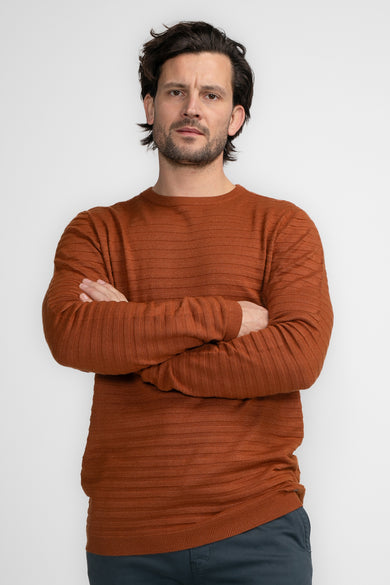Pull à col rond cognac de Petrol Industries® avec texture côtelée et manches longues, porté avec un pantalon bleu marine.