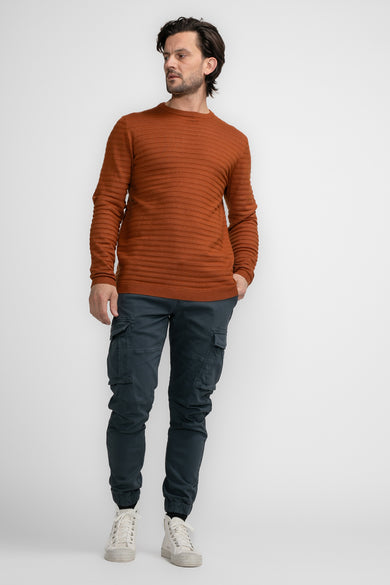 Pull à col rond cognac de Petrol Industries, avec une texture côtelée, porté avec un pantalon cargo et des chaussures de sport.