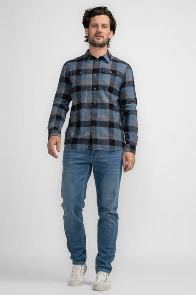 Chemise à manches longues bleue à carreaux par Petrol Industries®, portée avec un jean décontracté et des baskets blanches.
