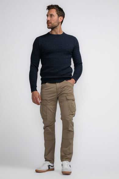Pantalon cargo beige par Petrol Industries® avec poches latérales, porté avec un pull bleu marine et des baskets blanches.