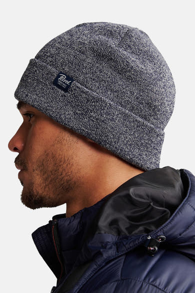 Bonnet bleu chiné de Petrol Industries, porté par un homme vu de profil, avec une veste matelassée marine.
