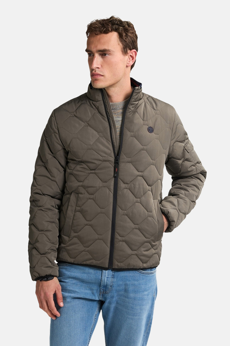 Korte grijze jas van Petrol Industries, gewatteerd met ruitpatroon, gedragen met een trui en een blauwe jeans.