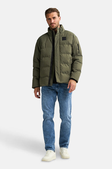 Groene regenjas van Petrol Industries, gedragen met een blauwe jeans en witte sneakers.