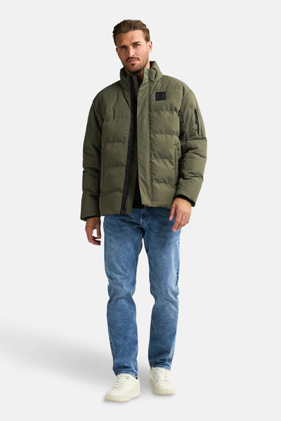 Groene regenjas van Petrol Industries, gedragen met een blauwe jeans en witte sneakers.