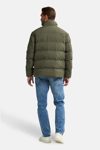 Groene regenjas van Petrol Industries, gedragen met een blauwe jeans en witte sneakers, achteraan gezien.