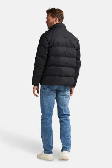 Veste de pluie noire de Petrol Industries, avec un design matelassé, portée avec un jean bleu et des baskets crème.