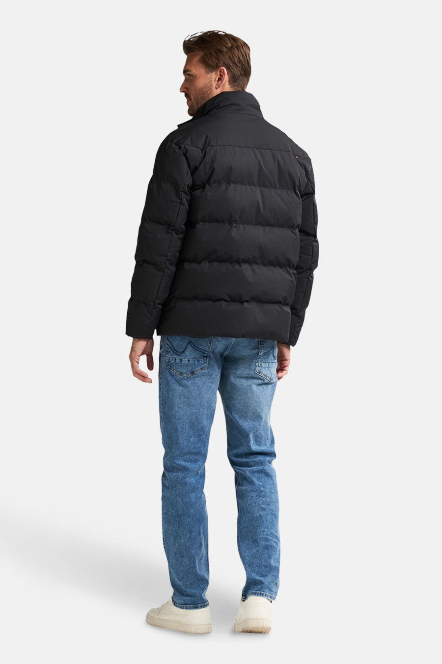 Veste de pluie noire de Petrol Industries, avec un design matelassé, portée avec un jean bleu et des baskets crème.