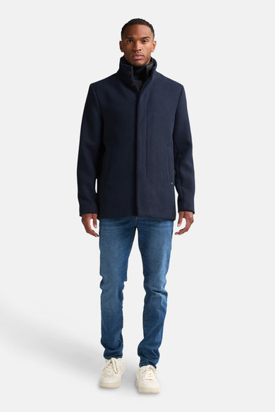 Blauwe jas van Petrol Industries, gedragen over een zwarte coltrui en een blauwe jeans met witte schoenen.