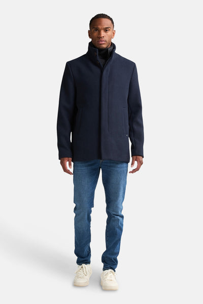 Blauwe jas van Petrol Industries, gedragen over een zwarte coltrui en een blauwe jeans met witte schoenen.