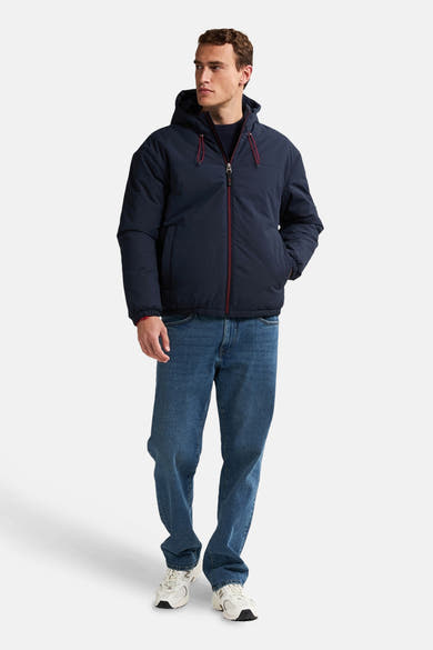Veste courte bleu marine par Petrol Industries® avec capuche et fermeture éclair rouge, portée avec un jean et des chaussures blanches.