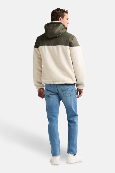 Groene regenjas van Petrol Industries, met capuchon, beige sherpa voering en blauwe jeans.
