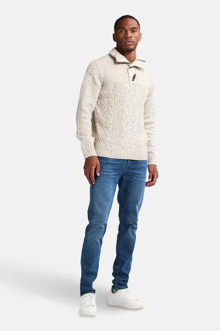 Ecru trui van Petrol Industries, met kabels en opstaande kraag, gedragen met een blauwe jeans en witte sneakers.