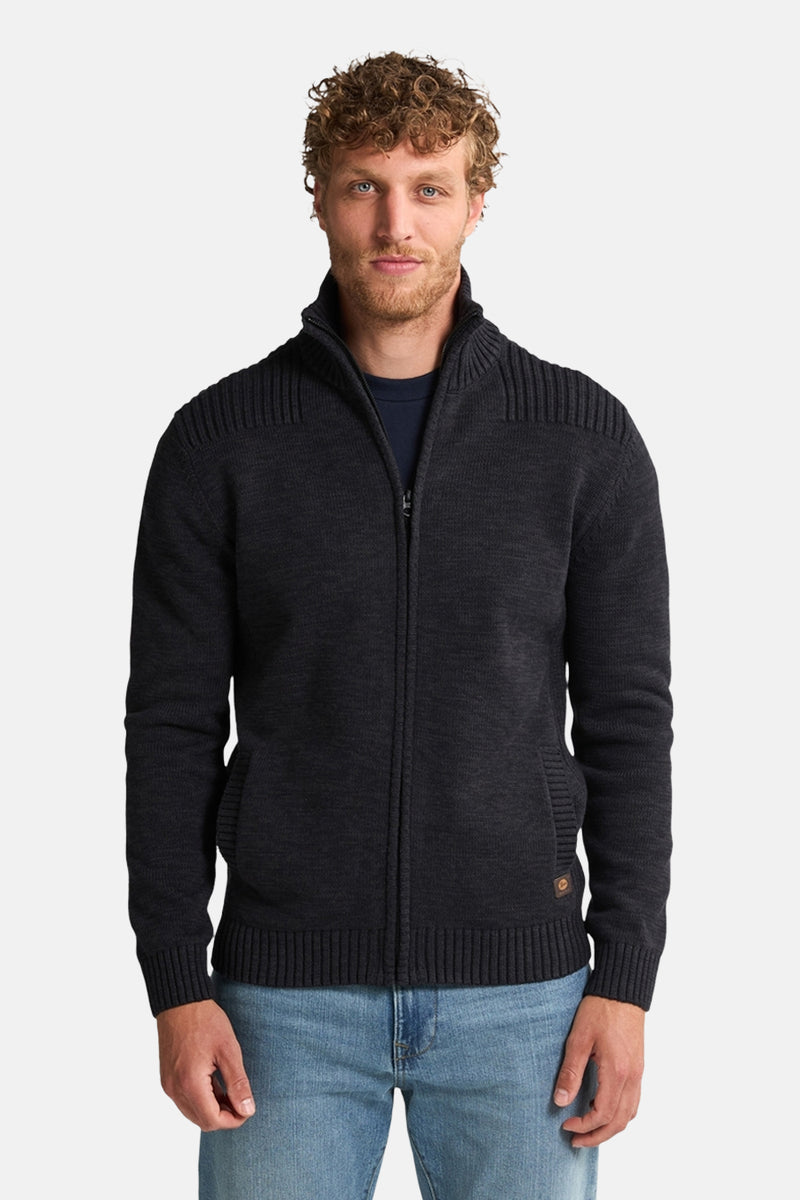 Zwart gewatteerd vest met rits van Petrol Industries, met textuur op de schouders en voorzakken, gedragen over een marineblauw T-shirt en een blauwe jeans.
