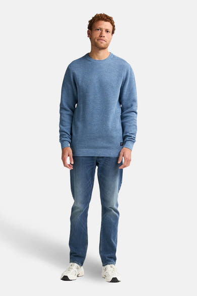 Ronde hals trui blauw van Petrol Industries, gedragen met een spijkerbroek en witte sneakers.