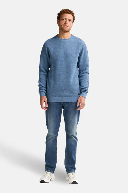 Ronde hals trui blauw van Petrol Industries, gedragen met een spijkerbroek en witte sneakers.