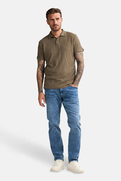 Groen poloshirt met korte mouwen van Petrol Industries®, gedragen met een blauwe jeans en witte sportschoenen.