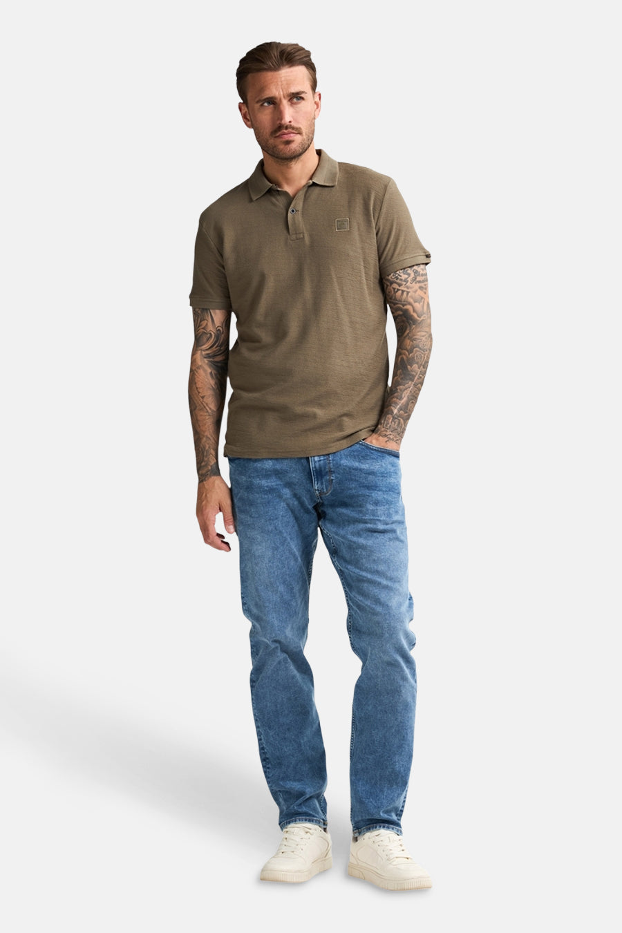 Groen poloshirt met korte mouwen van Petrol Industries®, gedragen met een blauwe jeans en witte sportschoenen.