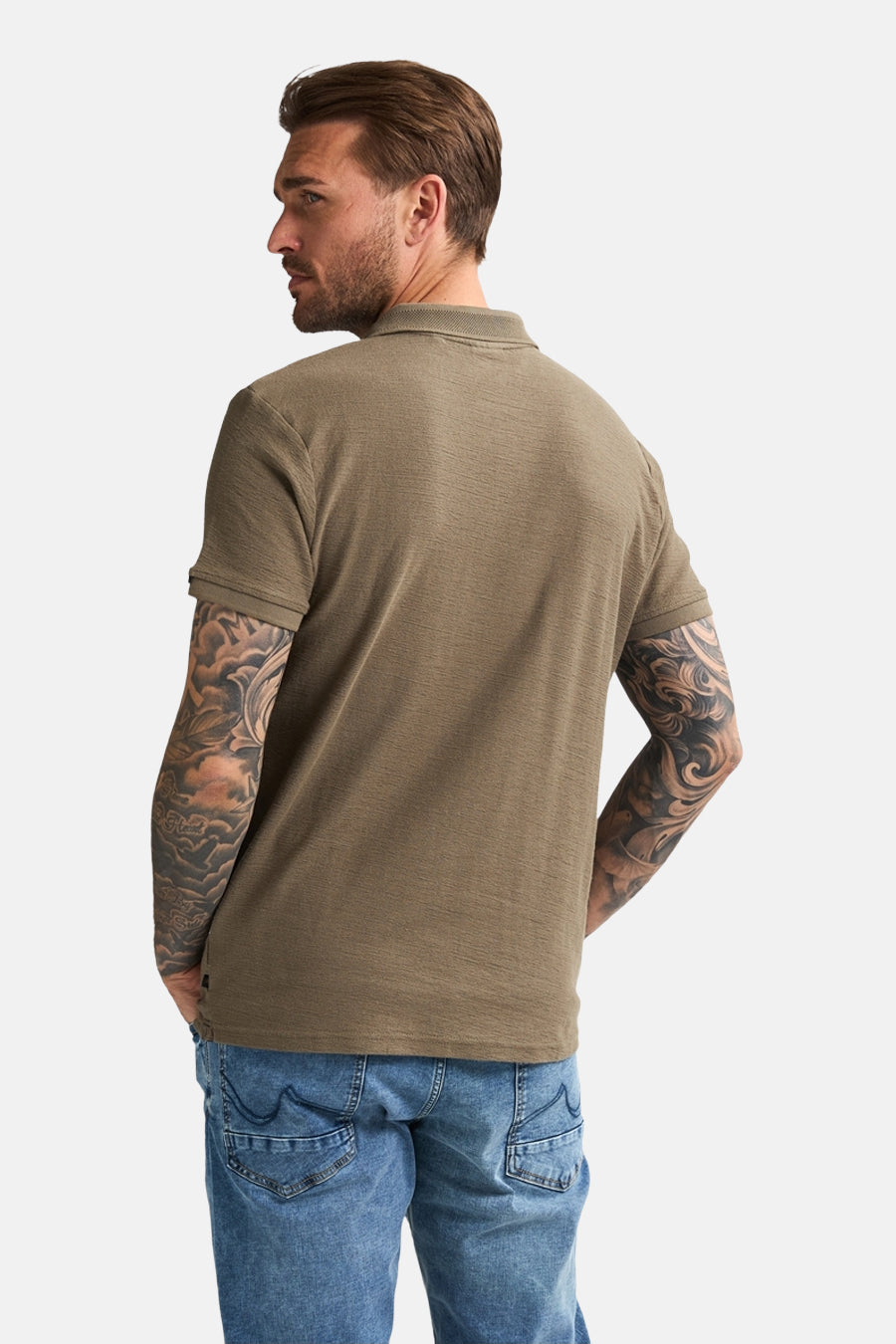Groen poloshirt met korte mouwen van Petrol Industries®, gedragen met een blauwe spijkerbroek en tatoeages op de armen.