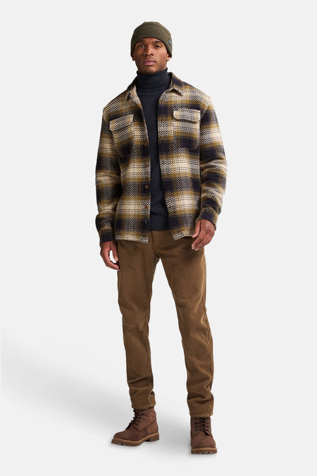 Blauw overhemd met lange mouwen van Petrol Industries, geruit, gedragen met een bruine broek en een olijfgroene muts.
