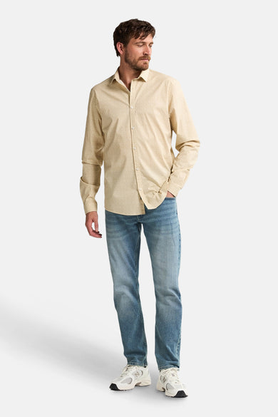 Chemise à manches longues beige de Petrol Industries, portée avec un jean bleu et des baskets blanches.