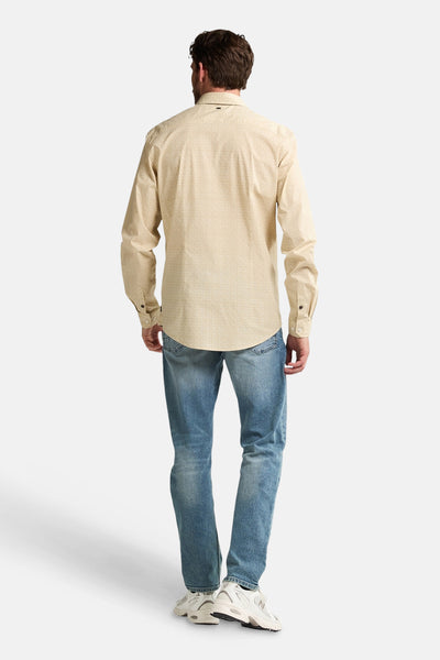 Chemise à manches longues beige de Petrol Industries, motif discret, portée avec un jean bleu et des baskets blanches.