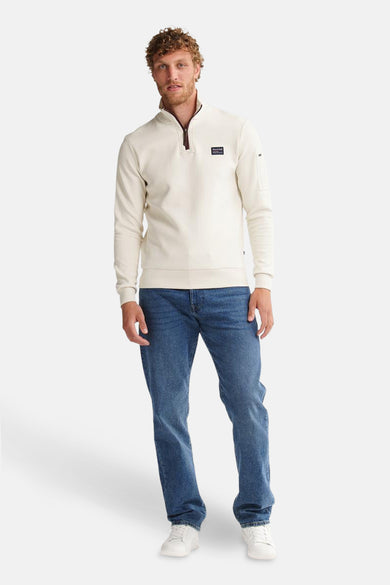 Ecru sweater met opstaande kraag van Petrol Industries, met ritssluiting en zak op de mouw, gedragen met een blauwe jeans.