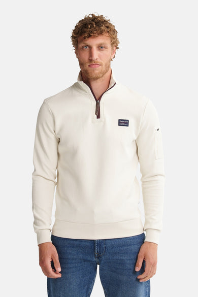 Ecru sweater met opstaande kraag van Petrol Industries, met ritssluiting en logopatch, gedragen met een blauwe jeans.