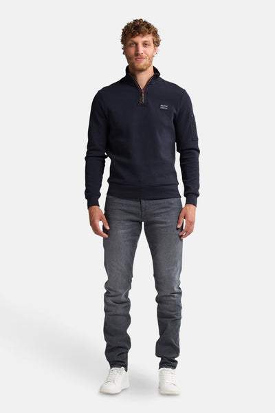 Blauwe sweater met opstaande kraag van Petrol Industries, gedragen met een grijze jeans en witte sneakers.