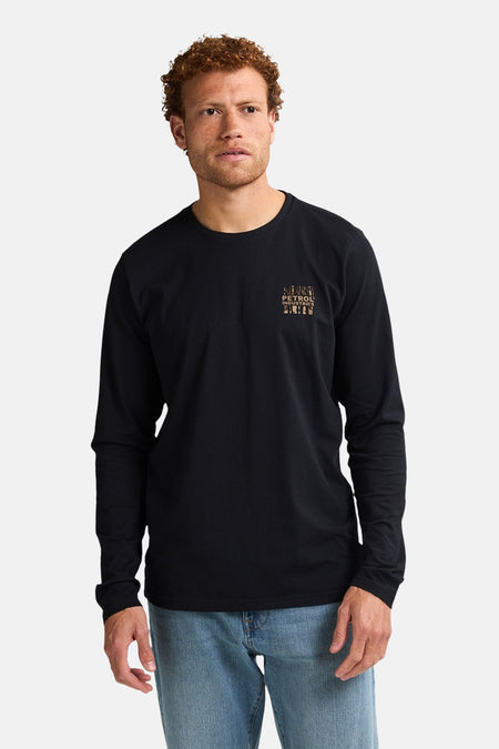 Zwart T-shirt met lange mouwen van Petrol Industries, met een klein grafisch logo op de borst, gedragen met een spijkerbroek.