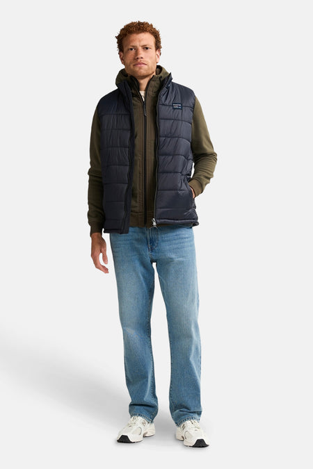 Zwart mouwloos jack van Petrol Industries, gedragen met een olijfgroene hoodie en een blauwe jeans.
