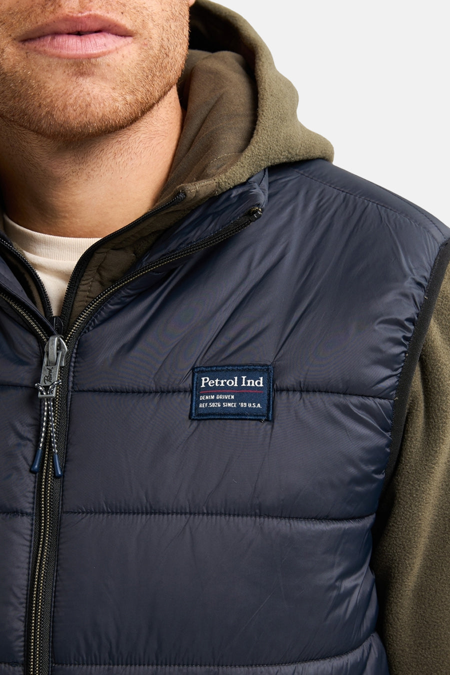 Zwarte mouwloze jas van Petrol Industries met ritssluiting, over een olijfgroene hoodie.