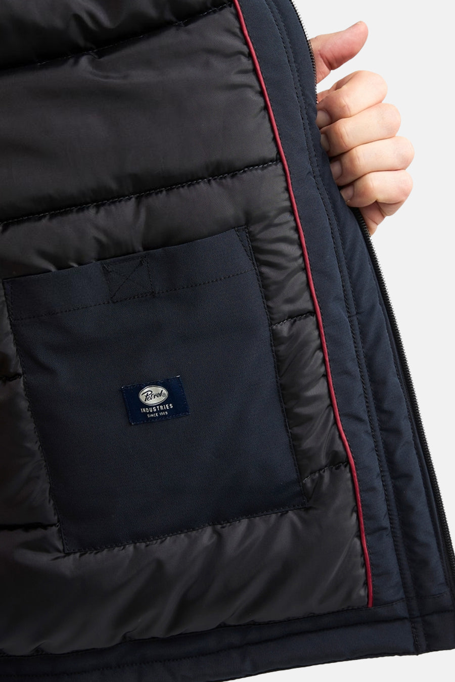 Black long puffer vest by Petrol Industries with quilted texture, red zipper trim, and front pocket detail, side view close-up