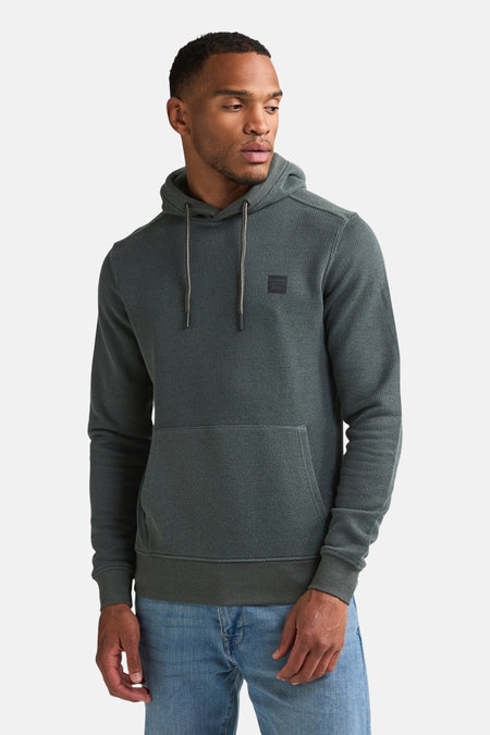 Green textured hoodie with front pocket and drawstrings by Petrol Industries, worn by model in side view with blue jeans.