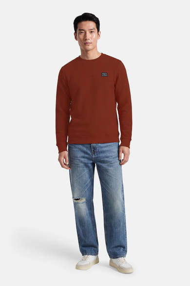 Rouge textured crewneck sweatshirt with ribbed cuffs and small chest patch, worn with distressed jeans and white sneakers, front view