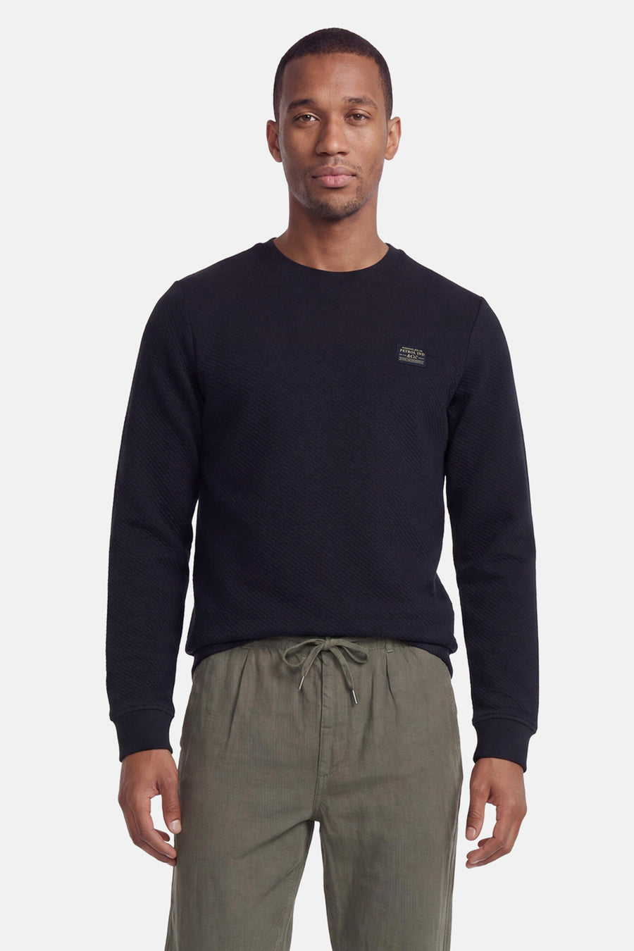Navy blue ribbed crewneck sweatshirt by Petrol Ind, featuring small chest patch, worn with olive green drawstring pants, front view.