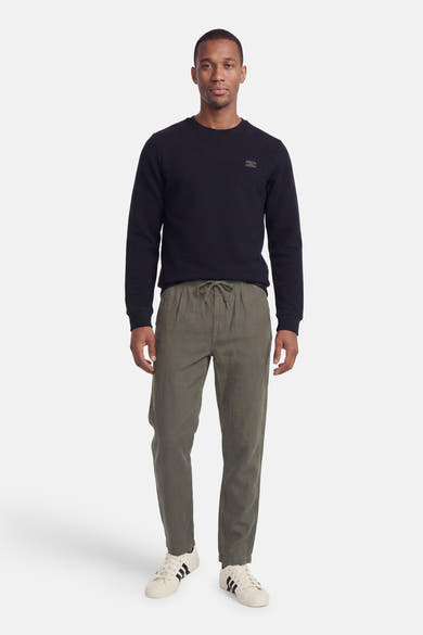 Navy blue ribbed crewneck sweatshirt with small chest patch, worn with olive green drawstring pants and white sneakers, front view