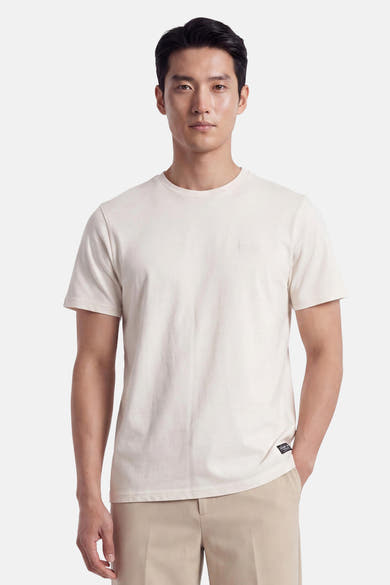 Ecru short-sleeve t-shirt with round neckline and small chest logo, worn by model in front view, paired with beige trousers
