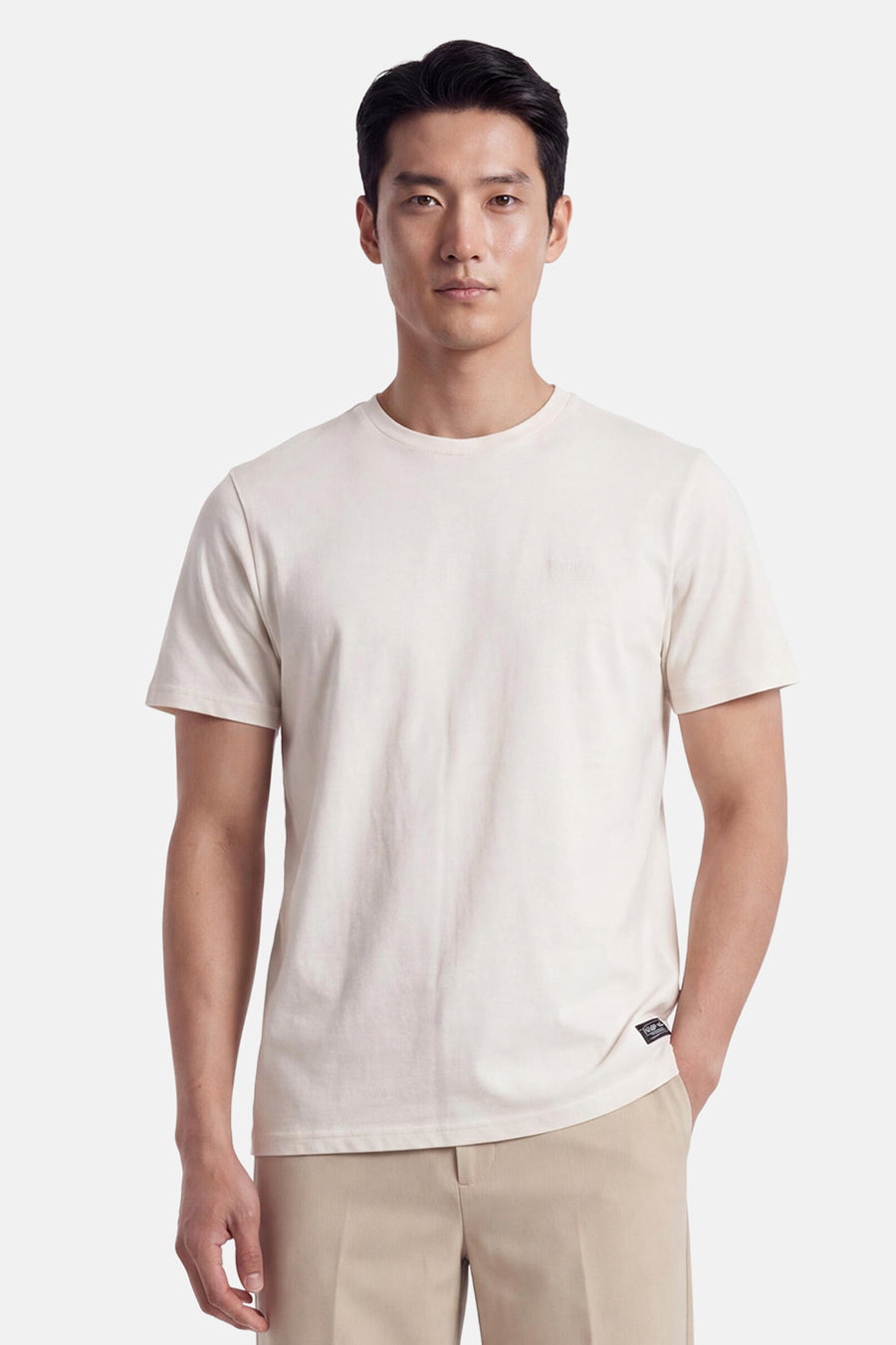 Ecru short-sleeve t-shirt with round neckline and small chest logo, worn by model in front view, paired with beige trousers