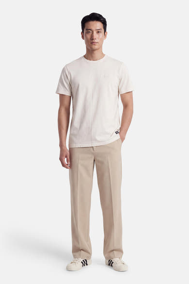 Ecru short-sleeve t-shirt with round neckline and small chest logo, worn by model in full-length front view with beige trousers and white sneakers.