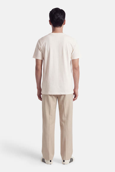 Ecru short-sleeve t-shirt from back view, plain cotton fabric, worn with beige trousers and striped sneakers