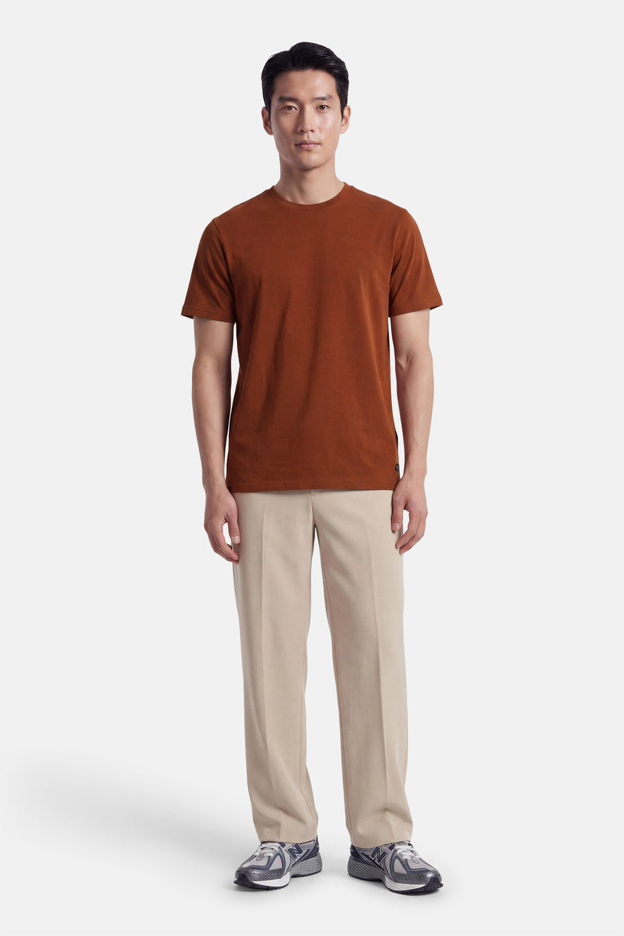 Orange short-sleeve t-shirt with round neckline and small chest logo, worn by model in full-length front view with beige trousers and sneakers.