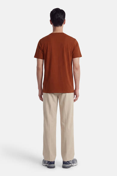 Orange short-sleeve t-shirt back view, solid color, soft cotton texture, worn with beige trousers and sneakers.
