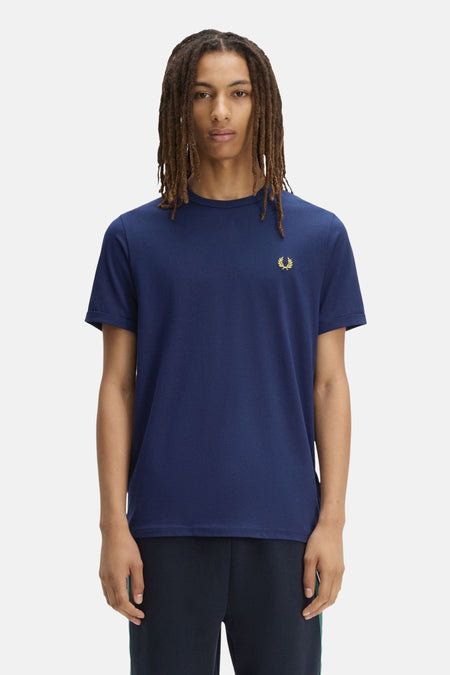 Marineblauwe T-shirt van FRED PERRY met gouden lauriertaklogo op de linkerborst, gedragen door een man.