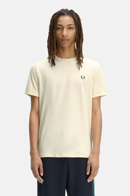 Ecru T-shirt van FRED PERRY met een groen lauriertaklogo, gedragen door een man met dreadlocks en een marineblauwe broek.