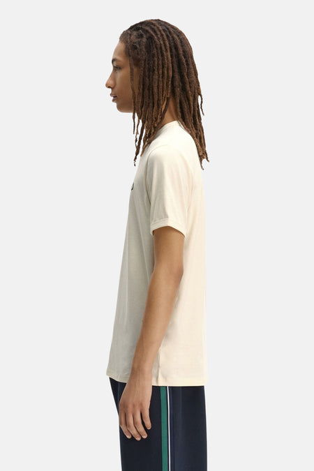 Ecru T-shirt van FRED PERRY, van opzij gezien op een man met dreadlocks die een marineblauwe joggingbroek draagt.